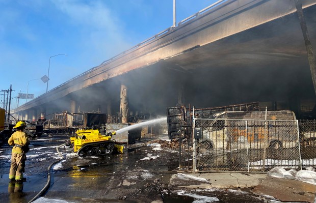 In this photo provided by the California Department of Transportation, a Los Angeles firefighter uses a robotic hose to douse a fire under Interstate 10 that severely damaged the overpass in an industrial zone near downtown Los Angeles, Saturday, Nov. 11, 2023. Authorities say firefighters have mostly extinguished a large blaze that burned trailers, cars and other things in storage lots beneath a major highway near downtown Los Angeles, forcing the temporary closure of the roadway. (Caltrans District 7 via AP)