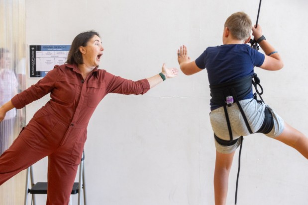 OAKLAND, CA - NOVEMBER 12: Taylor Samuelson of Oakland (left) hi-fives her son Elliot Smith while he hangs from a rope attached to a harness during a flight test vertical dance lesson at the BANDALOOP open house at their studio space in Oakland, Calif. on Nov. 12, 2023. BANDALOOP is a renown vertical dance troupe, that have performed their aerial mid-air performances on international landmarks around the world. (Douglas Zimmerman/Special to the Bay Area News Group)