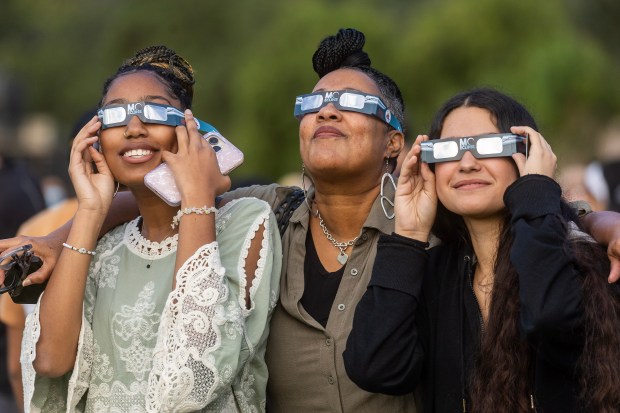 Lesley and Lyric Dawson, left and center, and Iyanis Ludwig use their special glasses to view the eclipse during a viewing event, Saturday, Oct. 14, 2023, at Stanford University. (Karl Mondon/Bay Area News Group)